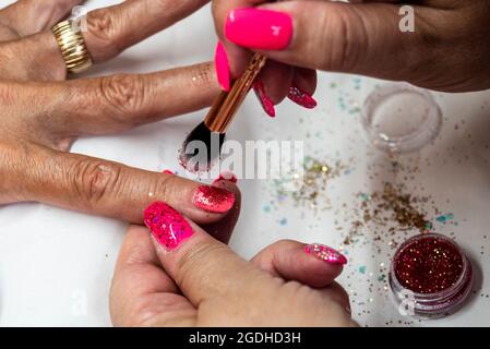 Application of soft gel nail treatment by a nail technician. Nail salon. Pink gel with glitter. Self employed working from home, authentic situation Stock Photo