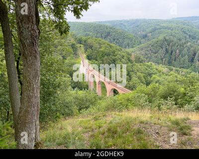 A path with trees on the side of a mountain with a bridge in the background. Stock Photo
