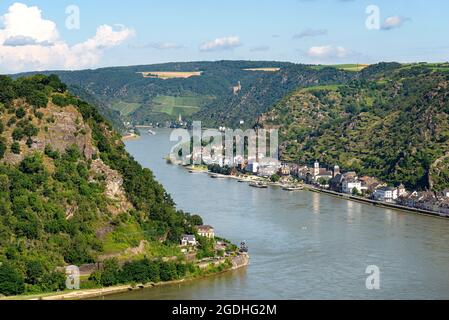 The river Rhine in western Germany flows between the hills covered with forest, visible buildings and a rock cliff. Stock Photo