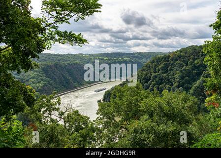 The river Rhine in western Germany flows between the hills covered with forest, visible barge and woods. Stock Photo