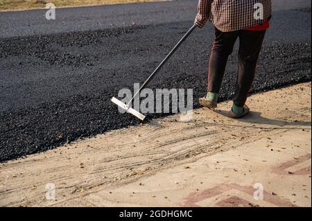 Construction worker using tool spread the hot-mix asphalt road accurately level covering on damaged highway Stock Photo