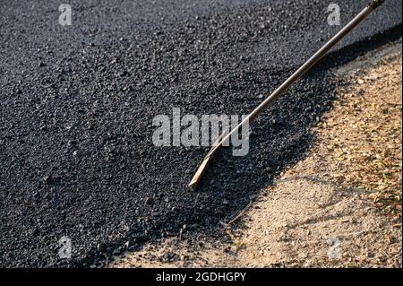 Construction worker using tool spread the hot-mix asphalt road accurately level covering on damaged highway Stock Photo