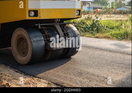 Yellow steamroller or soil compactor working on asphalt highway road at construction site Stock Photo