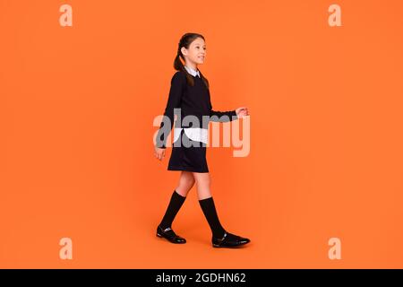 Full body photo of cheerful dreamy happy small girl look walk empty space isolated on orange color background Stock Photo