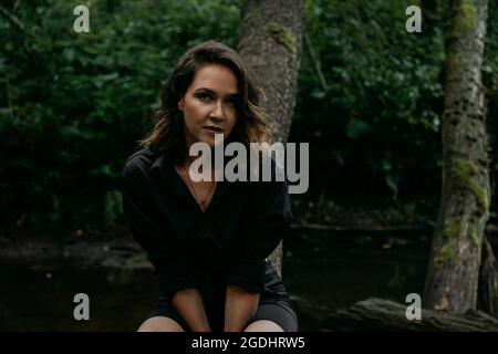 Young woman - close portrait in a dark pine forest. Woman in black shirt Stock Photo