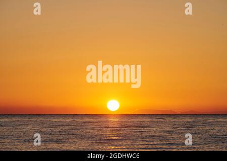 Bright sun rising on cloudless orange sky over rippling sea water in morning in Iceland Stock Photo