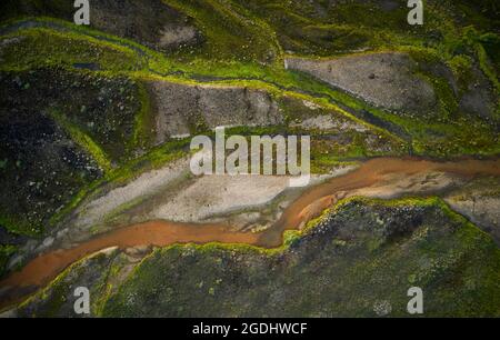 Aerial view of curvy river with orange water flowing between coasts covered with moss in highlands of Iceland Stock Photo