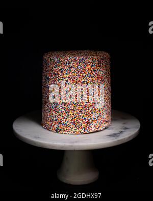 rainbow sprinkle cake on white marble cake stand Stock Photo