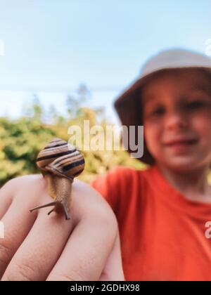 Snail on hand of smiling little boy outdoors close up Stock Photo