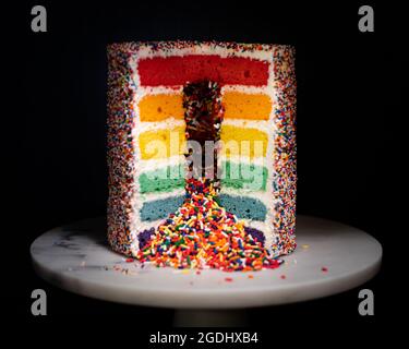 rainbow sprinkle layer cake on white marble cake stand Stock Photo