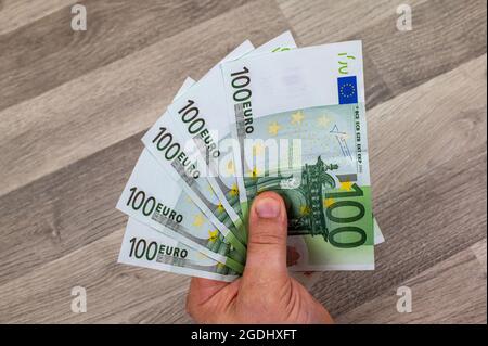 man hand holding 100 euro banknotes fan out over wooden table Stock Photo