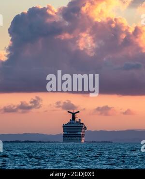 Coast of Belize - January 1, 2020: Carnival Conquest sailing by the coast of Belize at sunset. Blue ocean water in the foreground. Beautiful cloudy or Stock Photo