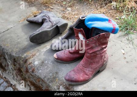 Old boots with a knitted cap are lined up on a low wall. Stock Photo