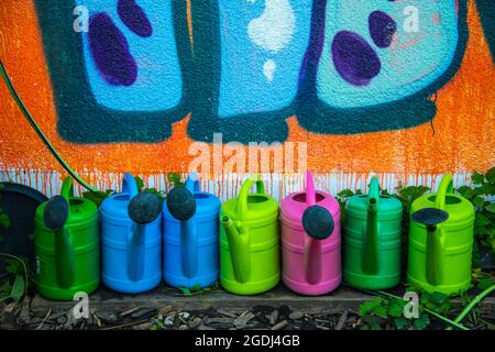 Many colorful water cans arranged in a row in the front of paint wall with graffiti Stock Photo