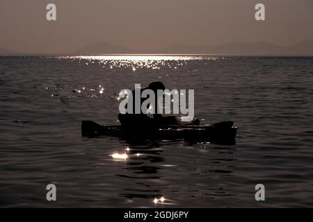 Fisherman in action. He stands in water and holds fly rod in one hand and  spoon in the other one. Also adult has a fishing net on the back. Green  Stock Photo - Alamy