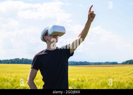 Man using virtual reality glasses outside in nature on a wheat farming field. Stock Photo
