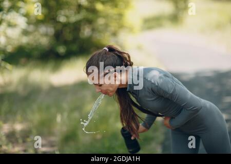 Tired runner woman jogger drinking bottled water after jogging