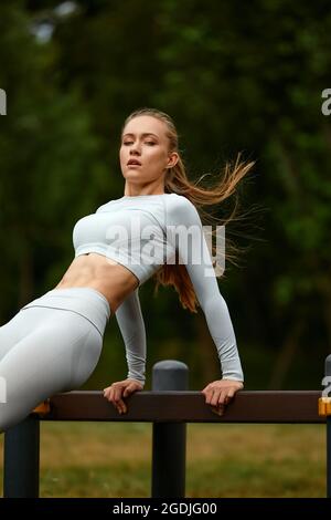 A blonde girl in a tracksuit trains in a park in an urban landscape, a