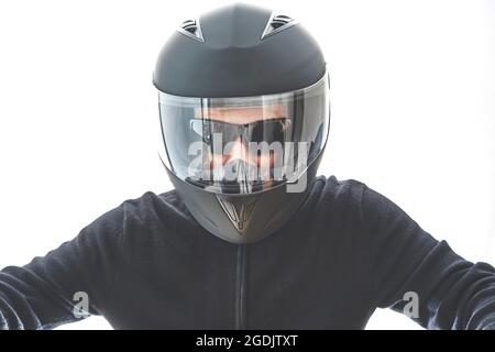 Portrait of guy with black checkered jacket and motorcycle helmet pretending to ride motorcycle, isolated on white studio wall. Stock Photo
