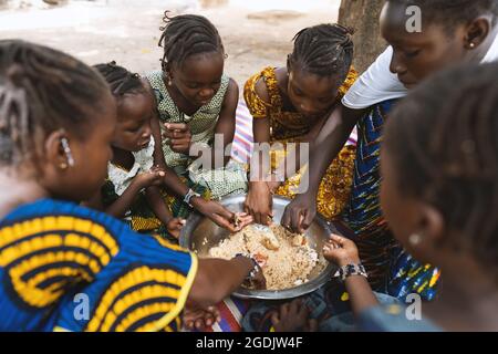 Group of African girls sitting around a big plate with rice and vegetables, enjoying their meal Stock Photo