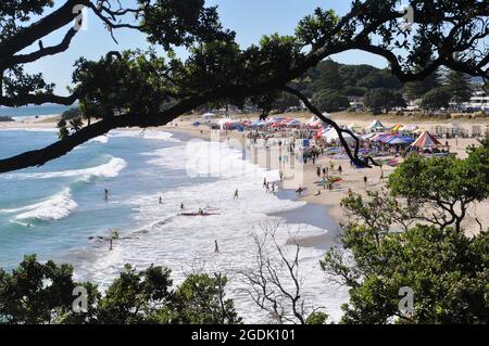A crowd of people enjoys the surf at Tauranga beach, New Zealand Stock Photo