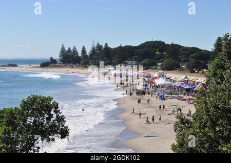 A crowd of people enjoys the surf at Tauranga beach, New Zealand Stock Photo