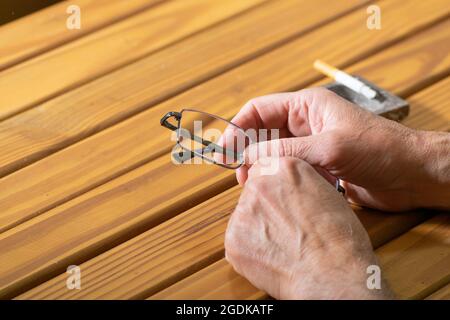 Hands holding reading glasses in front of an ashtray with a lit a cigarette Stock Photo