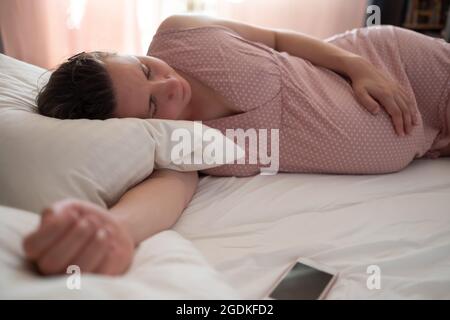 Sleeping pregnant caucasian woman in pink clothes on bed Stock Photo