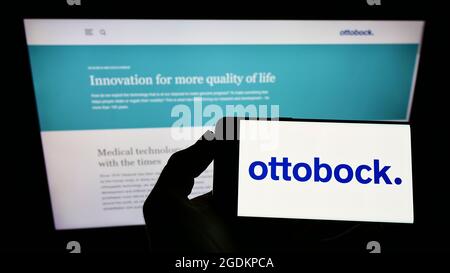 Person holding smartphone with logo of German prosthetics company Ottobock SE Co. KGaA on screen in front of website. Focus on phone display. Stock Photo