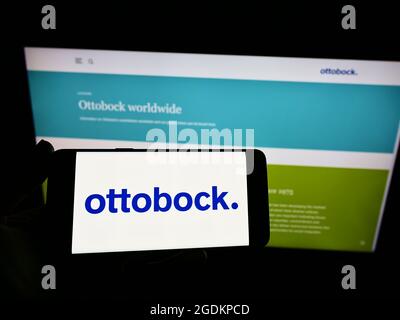 Person holding mobile phone with logo of German prosthetics company Ottobock SE Co. KGaA on screen in front of web page. Focus on phone display. Stock Photo