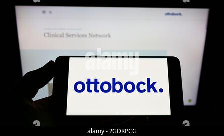 Person holding cellphone with logo of German prosthetics company Ottobock SE Co. KGaA on screen in front of webpage. Focus on phone display. Stock Photo