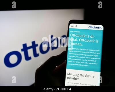 Person holding cellphone with webpage of German prosthetics company Ottobock SE Co. KGaA on screen with logo. Focus on center of phone display. Stock Photo