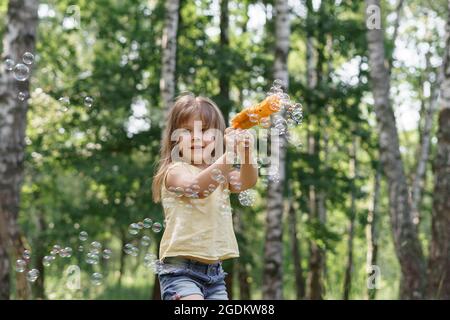 happy 5 year old girl blowing bubbles from a toy gun on a sunny summer day Stock Photo