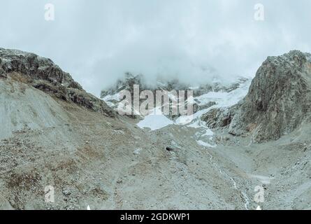 drone view over a desolate receding alpine glacier surrounded by mountains and snow covered rocks and peaks. Stock Photo