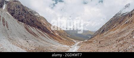 drone view over a desolate receding alpine glacier surrounded by mountains and snow covered rocks and peaks. Stock Photo