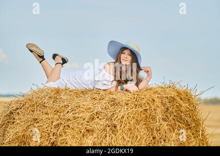 Pensive woman laying on the top of haystack on the field in sunny day Stock Photo