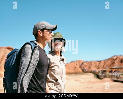 asian couple tourists backpackers walking chatting in national geological park, side view Stock Photo