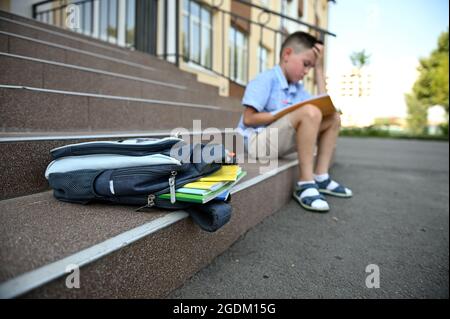 Back to school concept. Upset worried boy with backpack doing his homework. School bag with copy books and school supplies lying on the stairs. Back t Stock Photo