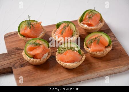 Tartlets with salmon, cheese, cucumber and dill. Tasty snacks with salted salmon and cottage cheese filling Stock Photo