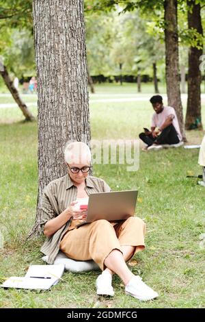 Young woman sitting on the grass and using laptop in her online study Stock Photo