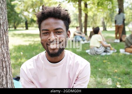 Portrait of African young man with curly hair smiling at camera while resting in the park outdoors Stock Photo
