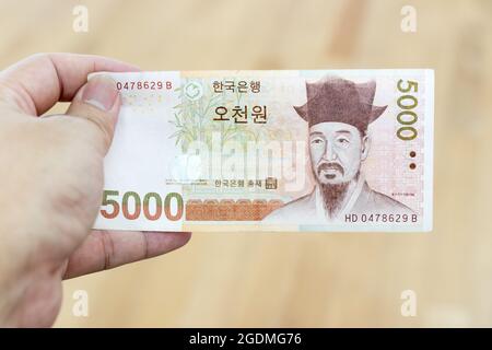 Business man hold south korea banknote 5000 korean won on wood background Stock Photo