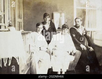 Two British Royal Navy salilors visiting two hospital patients sitting on a sofa by an open window. The sailor on the right has insgina of a Stoker, with two long service/good conduct stripes, and two medals. c. First World War. Stock Photo