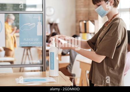Young woman in mask washing her hands with hand sanitizer before entering to the classroom at school Stock Photo
