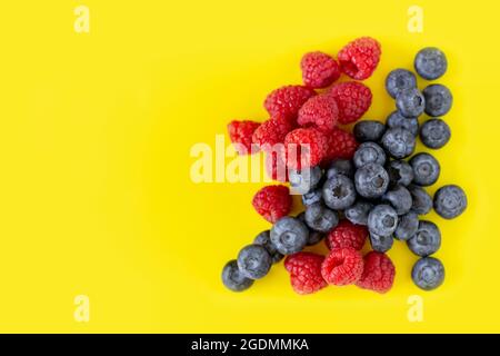 Delicious fresh organic blueberries and raspberries on bright yellow background with copy space. Stock Photo
