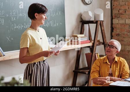 Student presenting her report to teacher during exam in the classroom at university Stock Photo