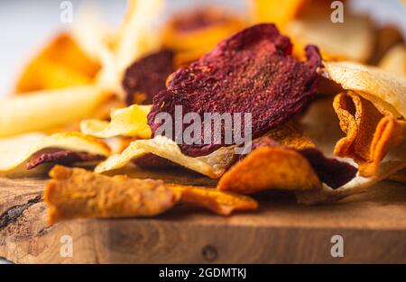 Vegetable chips from potatoes, beets and carrots laid on a wooden board close-up. Selective focus Stock Photo