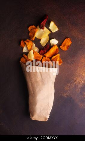 Vegetable chips made from potatoes, carrots and beets scattered from a kraft bag Stock Photo