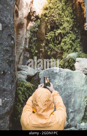 Rear view of hiker next to large red stone cave taking photo with smartphone Stock Photo