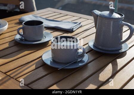 Gray ceramic teapot and pair of cups with five o'clock tea on a wooden table in a cafe. Tea time concept. Lifestyle background. Isometric style. Stock Photo